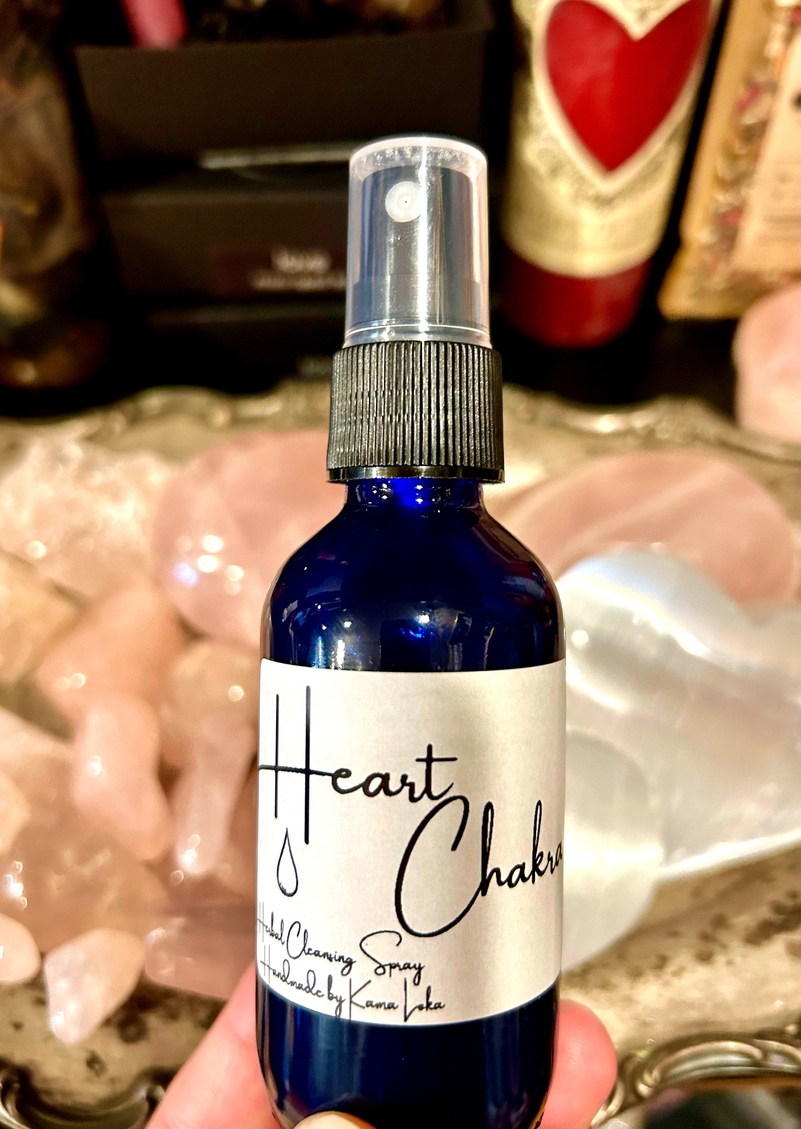 A blue spray bottle labeled 'Heart Chakra' with a white mask on the cap, held by a person with a blurred background.